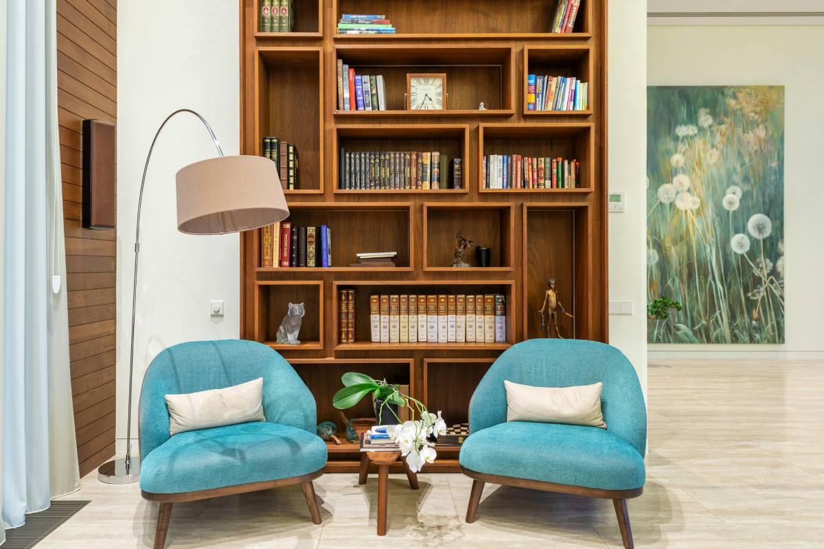 A cozy living room corner with two chairs, a round wood side table, wall shelves of books, and dried pampas grass — budget living room ideas