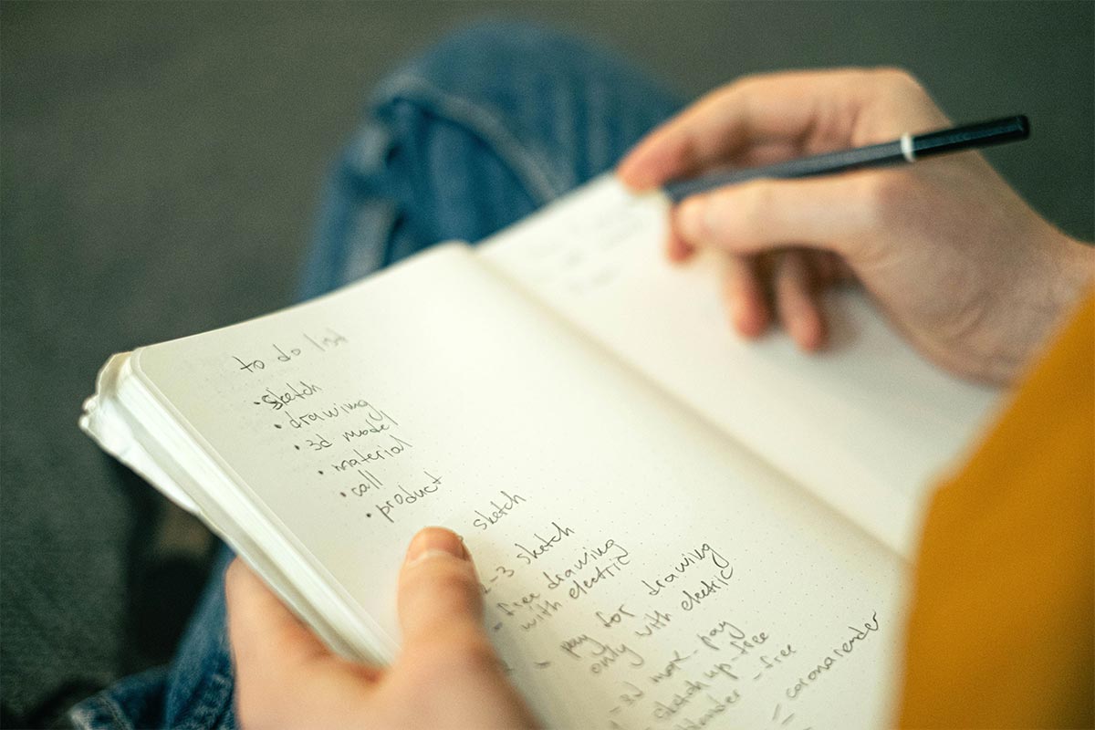A hand writing a want list in a Notes app and a spiral notebook instead of buying — how to stop impulse buying