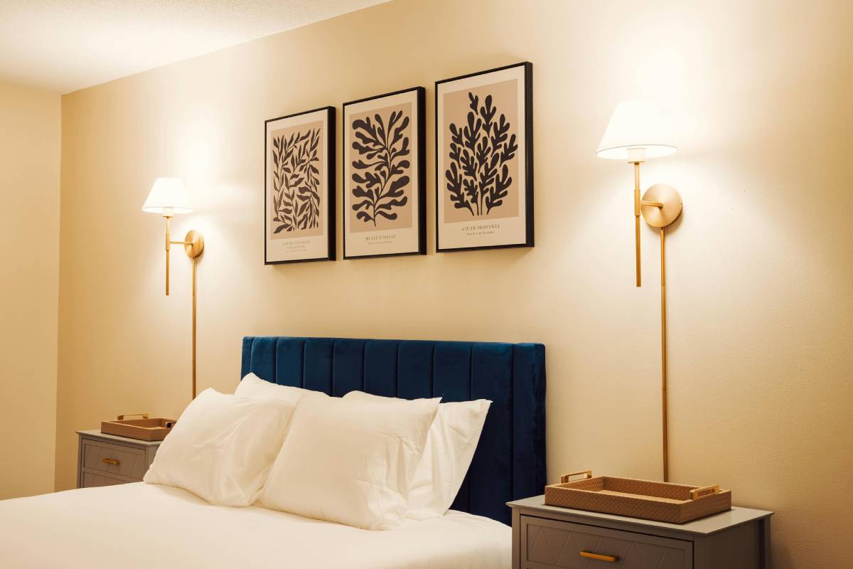 A thrifted wooden nightstand styled with a warm lamp, a stacked book, and a small plant beside a bed — affordable bedroom ideas on a budget