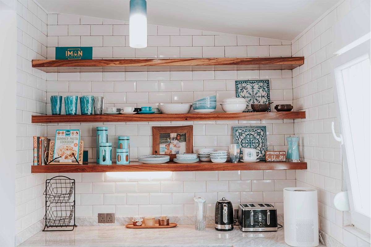 Open shelving in a small budget kitchen styled with a few plates, glass jars, and a potted herb on the windowsill β cheap kitchen decor