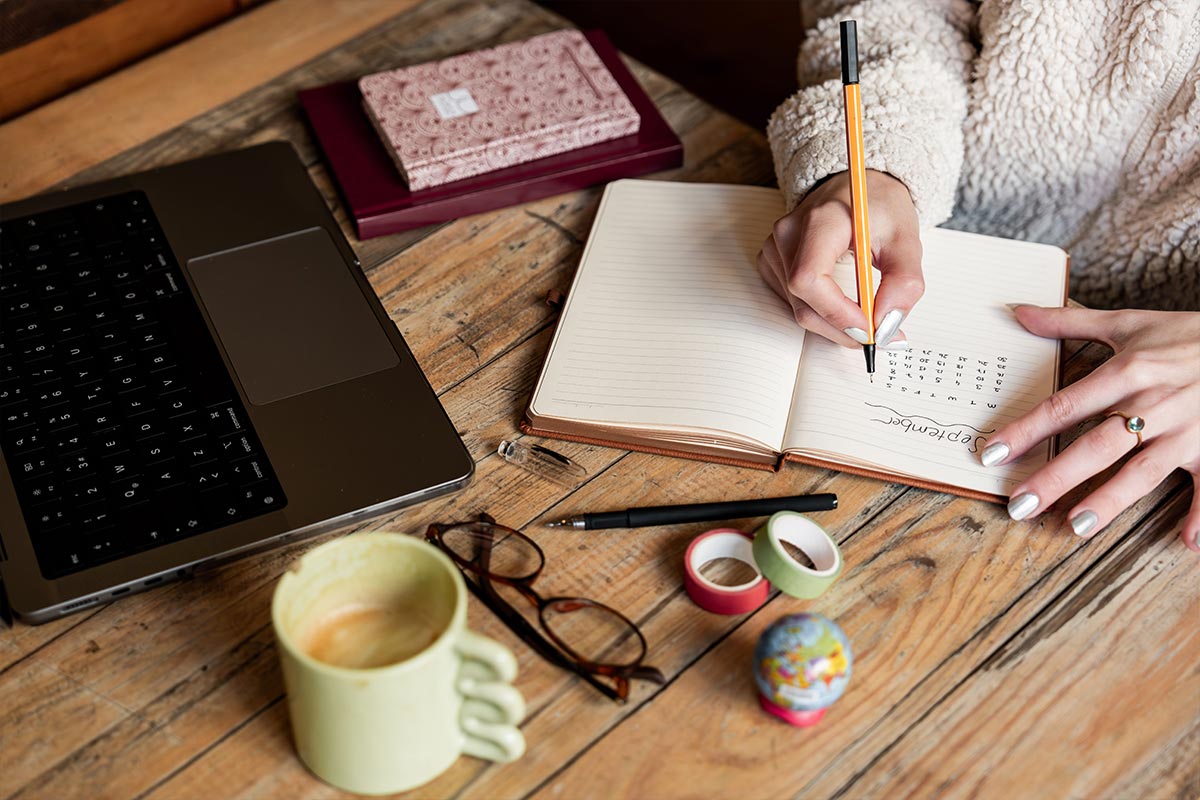 A woman writing a budget in a notebook beside a laptop and a coffee — budgeting for beginners at home