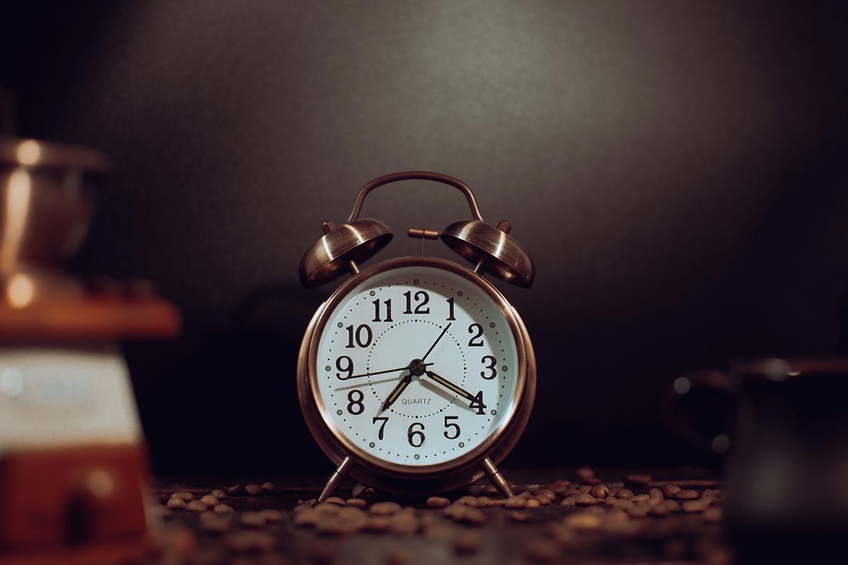 A vintage alarm clock among coffee beans in warm light, set to a consistent wake-up time — morning routine on a budget