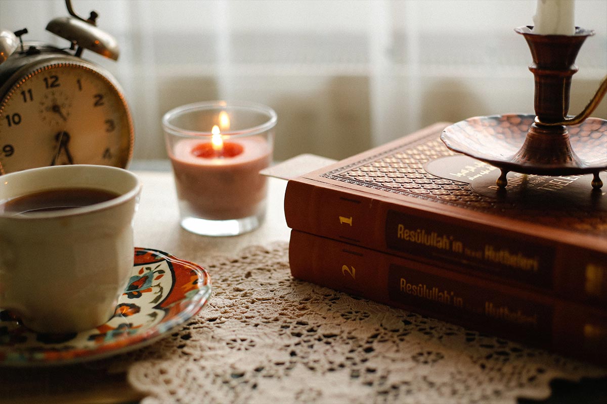 A lit candle, a mug of tea, and a book on a cozy table — low-cost self care ideas on a budget at home